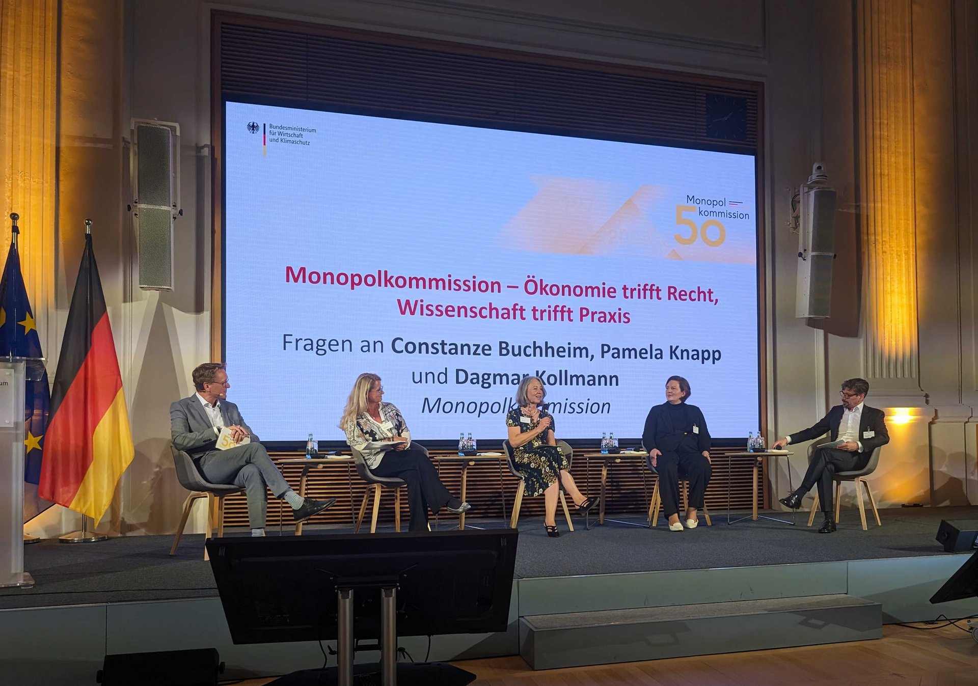 Die fünf Mitglieder der Kommission auf der Bühne, diskutierend auf einem Panel anlässlich 50 Jahre Monopolkommission